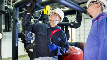 Two Sodexo employees wearing overalls, googles and hard hats, mending pipework